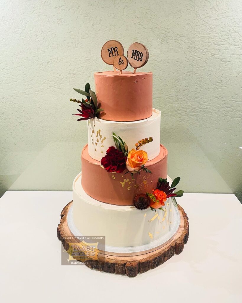 Vierlaagse bruidstaart in terracotta en wit met verse bloemen en een houten Mr & Mrs-topper