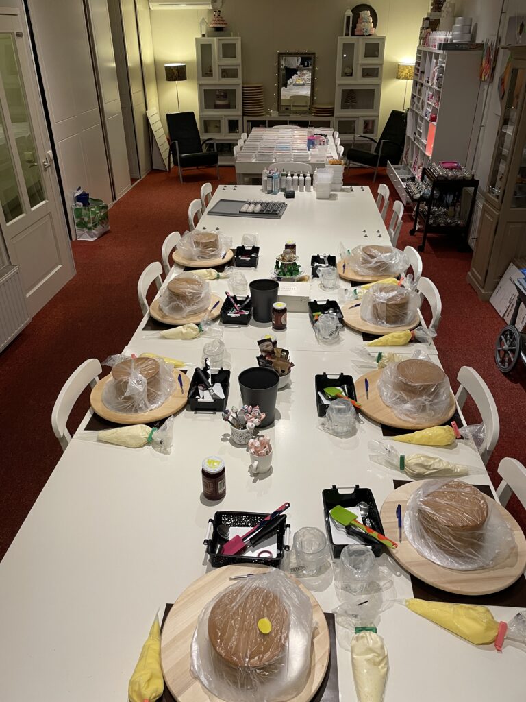 De workshoptafel is gedekt: op elke plek een taart op een draaiplateau, met spuitzakken en gereedschap klaar